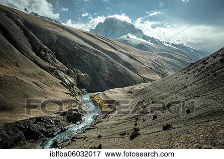 Stock Photo - Trough valley, barren scree landscape, riverbed of the Wachandarja, on the right mountain flank the caravan route through the Wakhan Corridor, in the background snow-covered summit of the Hindu Kush, Wakhan Corridor, Badakhshan, Afghanistan, Asia. Fotosearch