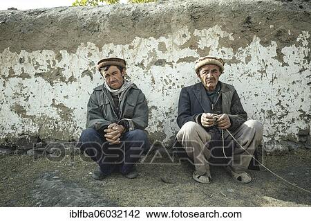 Two men squatting in front of a clay wall, sedentary Wakhi, Wakhan Corridor, Saradh-e-Broghil, Afghanistan, Asia View Large Photo Image Stock Image - Two men squatting in front of a clay wall, sedentary Wakhi, Wakhan Corridor, Saradh-e-Broghil, Afghanistan, Asia. Fotosearch