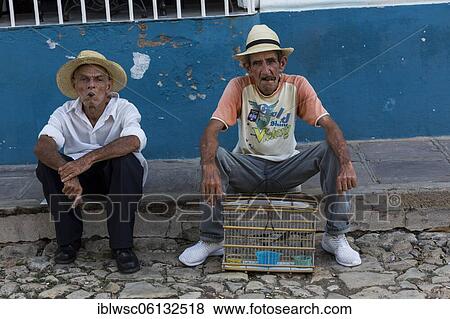 Stock Photo - Two older Cubans with cigars and songbird in a cage, Central America, Trinidad, Cuba, Central America. Fotosearch