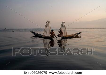 Stock Photo - Two traditional fishermen pose sitting on their small boats, at sunrise, Lake Inle, Myanmar, Asia. Fotosearch