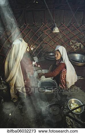 Stock Image - Two woman stirring dough for flat bread, in front of them a bucket and a teakettle on a fireplace, yurt, bozai gumbaz, wakhan corridor, Badakhshan, Afghanistan, Asia. Fotosearch