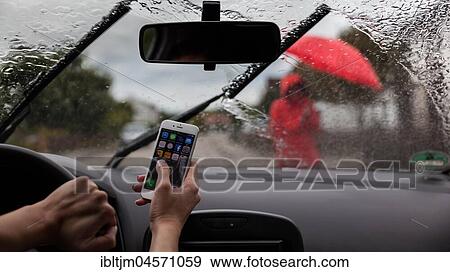 Woman sitting at the wheel of a car playing with mobile phone in rain, poor visibility, pedestrian on sidewalk, Germany, Europe View Large Photo Image Stock Photo - Woman sitting at the wheel of a car playing with mobile phone in rain, poor visibility, pedestrian on sidewalk, Germany, Europe. Fotosearch