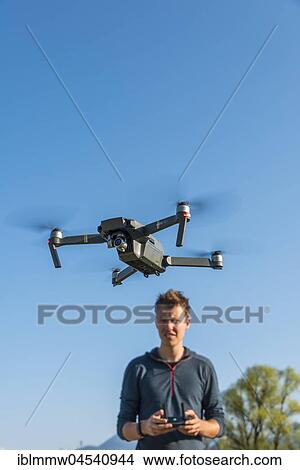 Young man controlling flying quadrocopter, remote controlled drone with camera, DJI Mavic View Large Photo Image Picture - Young man controlling flying quadrocopter, remote controlled drone with camera, DJI Mavic. Fotosearch