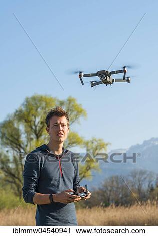 Stock Image - Young man controlling flying quadrocopter, remote controlled drone with camera, DJI Mavic. Fotosearch