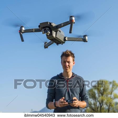 Stock Image - Young man controlling flying quadrocopter, remote controlled drone with camera, DJI Mavic. Fotosearch