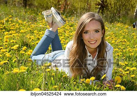 Picture - Young woman lying in a meadow of dandelion, Ystad, Scania, Sweden, Europe. Fotosearch