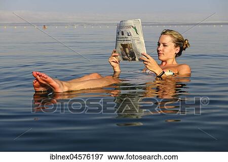 Stock Photo - Young woman reads newspaper floating in Dead Sea, Jordan, Asia. Fotosearch