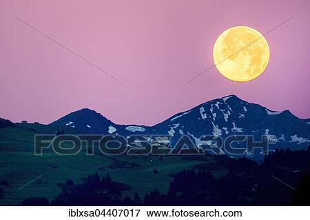 Stock Photo - Big full moon over the Swiss Alps, pink sky, Flims, Canton of Grisons, Switzerland, Europe. Fotosearch