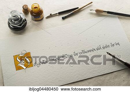 Stock Image - Calligraphy studio, hand writes text with pen and nib, letter S coated with gold and writing on torchon paper, hand embossing visible, inkwell and pen holder at back, Seebruck, Upper Bavaria, Germany, Europe. Fotosearch