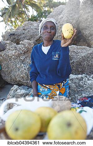 Stock Image - Female fruit vendor holding mango in her hand, 34 years old, Bamburi Beach, Mombasa, Mombasa County, Kenya, Africa. Fotosearch