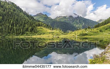 Stock Photo - Fisherman on Lake Riesachsee with reflection of forest and mountains, Rohrmoos-Untertal, Schladming Tauern, Schladming, Styria, Austria, Europe. Fotosearch