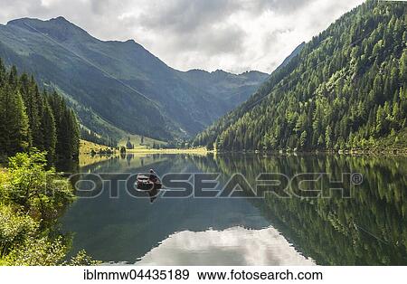 Stock Photo - Fisherman on Lake Riesachsee with reflection of forest and mountains, Rohrmoos-Untertal, Schladming Tauern, Schladming, Styria, Austria, Europe. Fotosearch