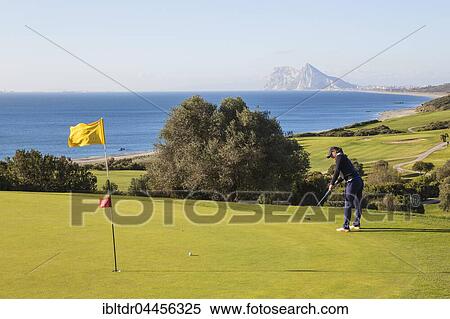 Stock Photography - Golfer putting on green, La Alcaidesa Golf Resort with Mediterranean Sea and Rock of Gibraltar, Cádiz, Andalusia, Spain, Europe. Fotosearch