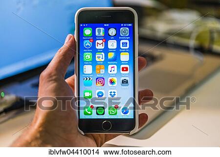 Hand holding iPhone 6S with home screen displaying multiple icons View Large Photo Image Picture - Hand holding iPhone 6S with home screen displaying multiple icons. Fotosearch