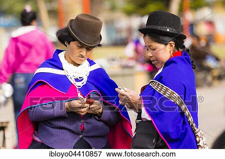 Stock Photo - Indigenous people, Guambiano women wearing traditional dress looking at mobile phones, Guambiano Indigenous Market, Silvia near Popayan, Cauca, Colombia, South America. Fotosearch
