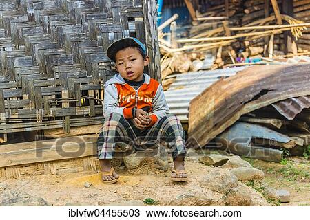 Stock Image - Little boy sitting in front of log cabin, Palaung hilltribe, Palaung Village in Kyaukme, Shan State, Myanmar, Asia. Fotosearch