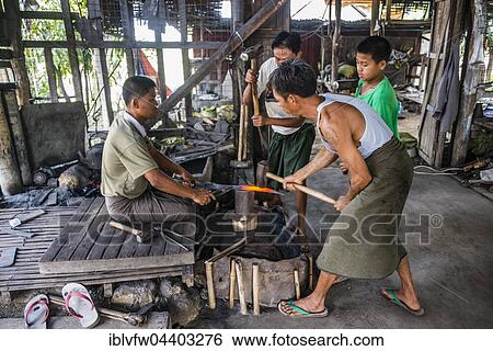 Stock Photograph - Local blacksmiths banging with hammers on glowing piece of metal, Inle Lake, Shan State, Myanmar, Asia. Fotosearch