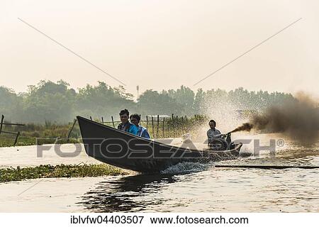 Stock Photo - Locals on wooden motor boat with dark smoke, Inle Lake, Shan State, Myanmar, Asia. Fotosearch