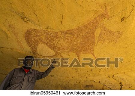 Stock Image - Man pointing out a Rock painting in the Unesco world heritage, Ennedi Plateau, Chad, Africa. Fotosearch