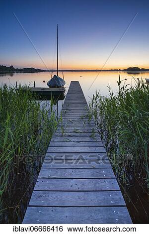 Morning glow at the Schaalsee, wooden jetty in the reeds with sailing boat, biosphere reserve Schaalsee, Mecklenburg-Western Pomerania, Germany, Europe View Large Photo Image Stock Photograph - Morning glow at the Schaalsee, wooden jetty in the reeds with sailing boat, biosphere reserve Schaalsee, Mecklenburg-Western Pomerania, Germany, Europe. Fotosearch