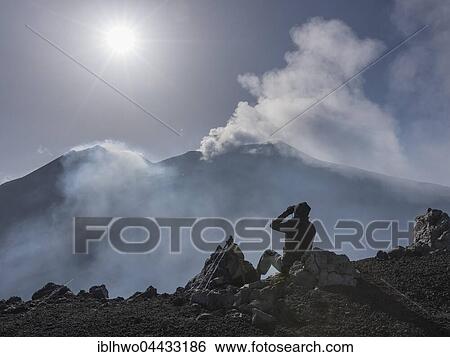 Mountain hiker looking at two fuming east craters in backlight, view from Rocca della Valle lookout point, Mount Etna, volcano, northeast flank, Sicily, Italy, Europe View Large Photo Image Stock Photograph - Mountain hiker looking at two fuming east craters in backlight, view from Rocca della Valle lookout point, Mount Etna, volcano, northeast flank, Sicily, Italy, Europe. Fotosearch