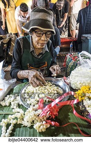 Stock Image - Old woman, Thai woman sells flowers and flower chains at the Night Market, Krabi Town, Krabi Province, Thailand, Asia. Fotosearch