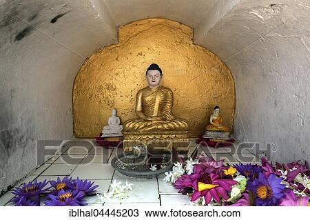 Stock Image - Small golden Buddha statue, Seated Buddha in prayer shrine with offerings, Weherahena Temple, Matara, Southern Province, Sri Lanka, Asia. Fotosearch