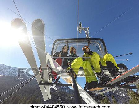 Stock Image - Three teenagers on chairlift with skis and snowboard, taking selfie, Spitzingsee ski resort, Bavaria, Germany, Europe. Fotosearch