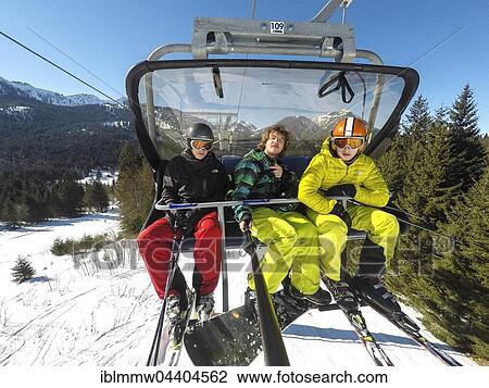 Stock Image - Three teenagers on chairlift with skis and snowboard, taking selfie, Spitzingsee ski resort, Bavaria, Germany, Europe. Fotosearch