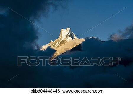 View on the summit of the mountain Machapuchare at sunset, partly covered by monsoon clouds, Chomrong, Kaski District, Nepal, Asia View Large Photo Image Stock Photograph - View on the summit of the mountain Machapuchare at sunset, partly covered by monsoon clouds, Chomrong, Kaski District, Nepal, Asia. Fotosearch