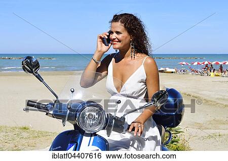 Woman in white dress and decorative earrings with cell phone on Vespa Primavera scooter on the beach, Senigallia, Adriatic Coast, Marche, Italy, Europe View Large Photo Image Stock Photograph - Woman in white dress and decorative earrings with cell phone on Vespa Primavera scooter on the beach, Senigallia, Adriatic Coast, Marche, Italy, Europe. Fotosearch