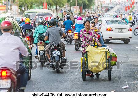 Woman pushing cart through scooter riders in heavy traffic, Ho Chi Minh City, Vietnam, Asia View Large Photo Image Picture - Woman pushing cart through scooter riders in heavy traffic, Ho Chi Minh City, Vietnam, Asia. Fotosearch