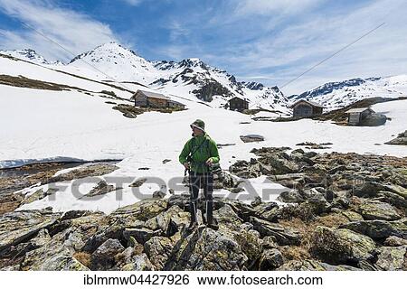 Stock Photograph - Young man, hiker standing in front of huts, Unterer Giglachsee, mountain landscape with residual snow, Rohrmoos Obertal, Schladming Tauern, Schladming, Styria, Austria, Europe. Fotosearch