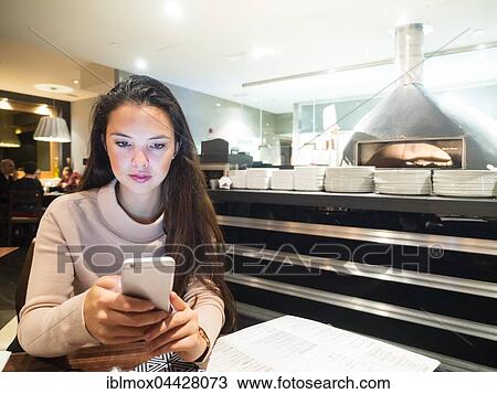 Stock Image - Young woman with mobile phone in a restaurant, London, England, United Kingdom, Europe. Fotosearch