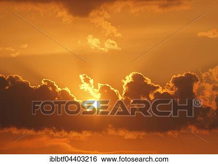 Stock Photograph - atmospheric sunset, sun behind dark clouds. Fotosearch