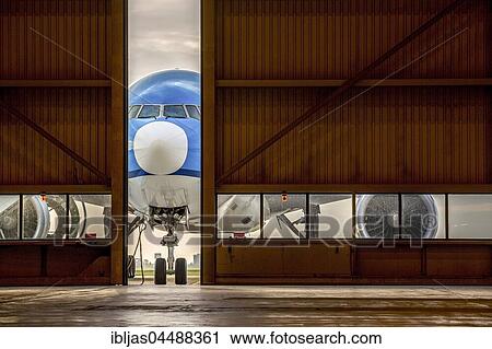 Stock Image - Blue airplane in front of half opened door to hangar, Schiphol Airport, Amsterdam, Netherlands. Fotosearch
