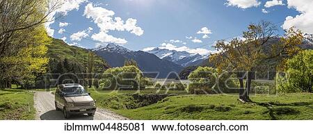 Stock Image - Car on road, Matukituki Valley, snowy Mount Aspiring, Mount Aspiring National Park, Otago, Southland, New Zealand, Oceania. Fotosearch
