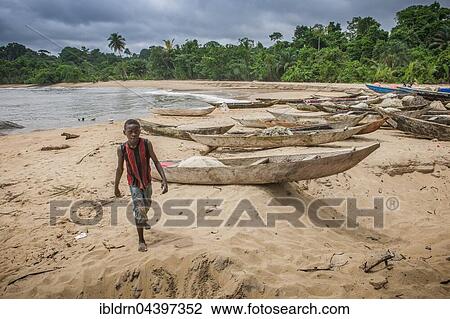 Stock Image - Child boy and dugout canoes on the beach, Ebodjé, Southern Region, Cameroon, Africa. Fotosearch