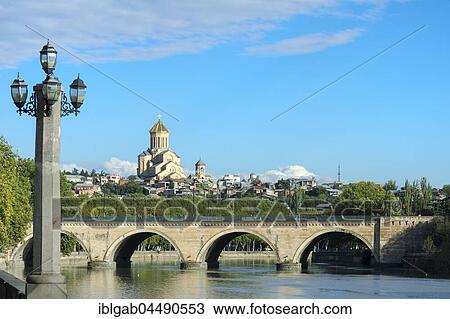 Stock Image - Chughureti or Saarbrucken bridge over Mtkvari river, Holy Trinity Cathedral on the hill, Tbilisi, Georgia, Asia. Fotosearch