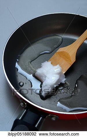 Stock Image - Coconut oil with bamboo spatula in frying pan. Fotosearch