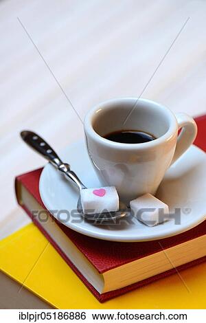 Stock Photograph - Coffee cup on books and coffee spoon with sugar cubes, espresso. Fotosearch