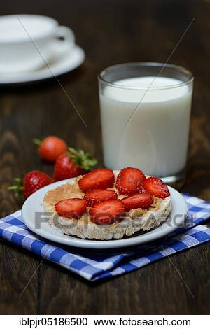 Stock Image - Corn and rice waffle topped with strawberries and peanut butter, glass of milk, cereal waffle. Fotosearch