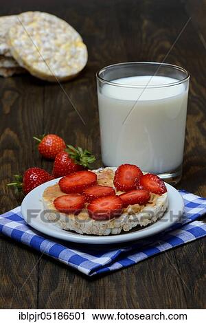 Stock Image - Corn and rice waffle topped with strawberries and peanut butter, glass of milk, cereal waffle. Fotosearch