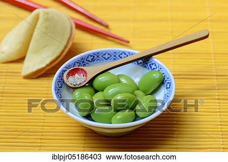 Stock Image - Edamame, cooked unripe Soya beans (Glycine max) in bowl, spoon with spiced salt Shichimi Togarashi. Fotosearch