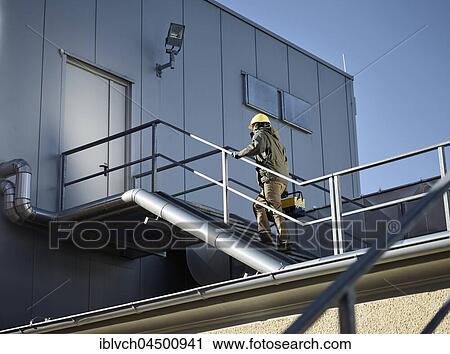 Stock Image - Engineer with yellow helmet and tool box using a staircase to an engine room, Austria, Europe. Fotosearch