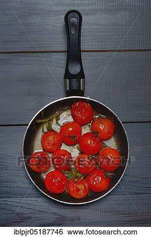 Stock Photograph - Fried cherry tomatoes with rosemary in pan, Solanum lycopersicum. Fotosearch