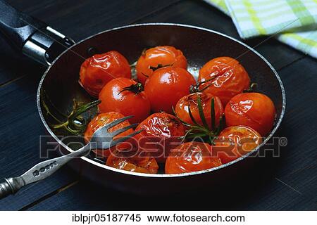 Stock Photography - Fried cherry tomatoes with rosemary in pan, Solanum lycopersicum. Fotosearch