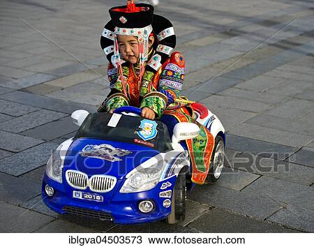 Stock Image - Girl in traditional Deel clothing driving a toy car, police car, Festival of the Mongolian national traditional costume, Ulaanbaatar, Mongolia, Asia. Fotosearch