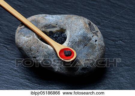 Stock Photograph - Hawaiian salt, black Hawaiian salt in stone with depression and spoon, with activated carbon, gourmet salt. Fotosearch