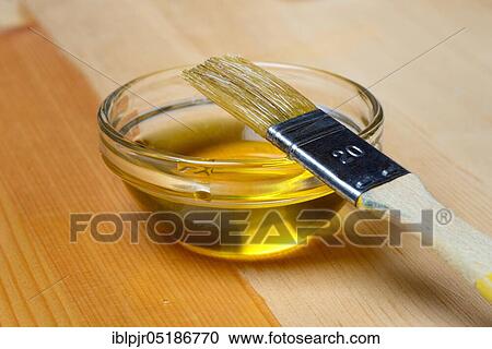 Stock Image - Linseed oil ( Linum usitatissimum) in bowl and brush, painting wood with linseed oil. Fotosearch